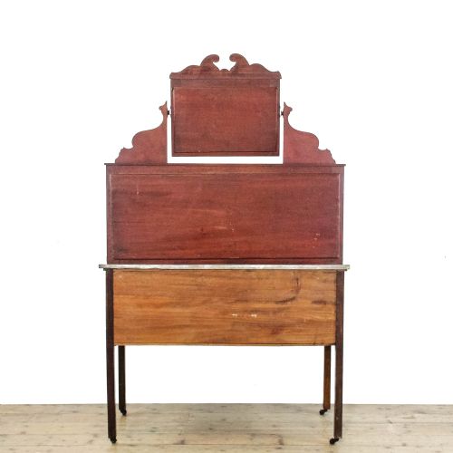 fig 2. An Edwardian mahogany washstand with a grey marble top, a green ceramic tiled splashback, and an arch-framed mirror above a two-door cabinet on castors.