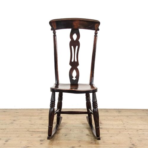 fig 1. An antique dark brown wooden rocking chair with a pierced central splat, turned legs, and a shaped seat set upon curved rockers.