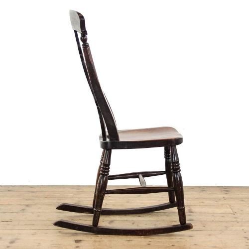 fig 2. An antique dark brown wooden rocking chair with a pierced central splat, turned legs, and a shaped seat set upon curved rockers.