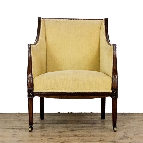 fig 1. An Edwardian armchair with pale yellow fabric upholstery, a dark mahogany frame with sweeping armrests, square tapered front legs, and brass castors.