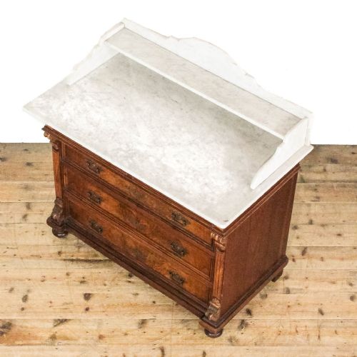 fig 1. An antique Continental chest of drawers featuring warm brown walnut veneers, brass handles, fluted side columns, and a white marble top with a gallery shelf.