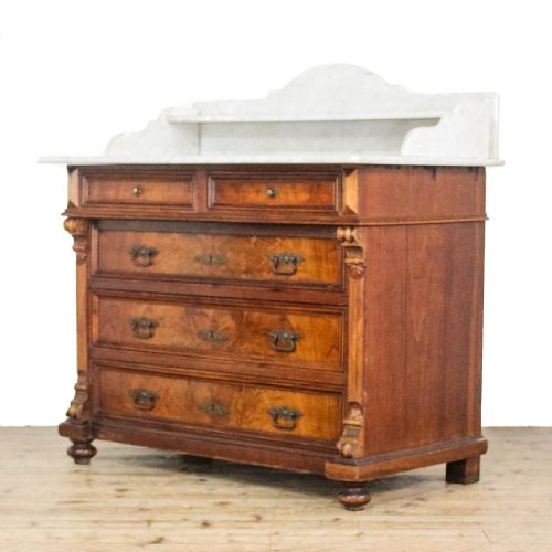fig 2. An antique Continental chest of drawers featuring warm brown walnut veneers, brass handles, fluted side columns, and a white marble top with a gallery shelf.