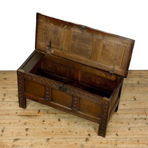 fig 2. An 18th-century dark oak coffer featuring three carved front panels, a carved floral frieze, a hinged top lid, and an iron lock plate.