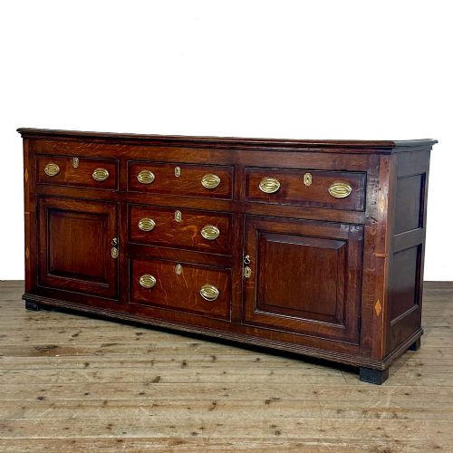 fig 1. An antique Georgian oak dresser base featuring brass oval drop handles, panelled cupboard doors, central drawers, and geometric diamond inlay.
