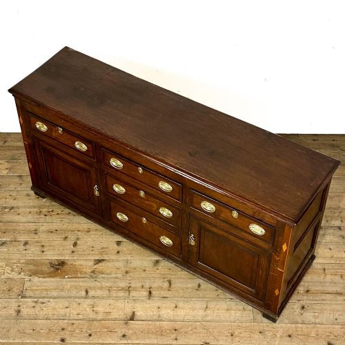 fig 2. An antique Georgian oak dresser base featuring brass oval drop handles, panelled cupboard doors, central drawers, and geometric diamond inlay.