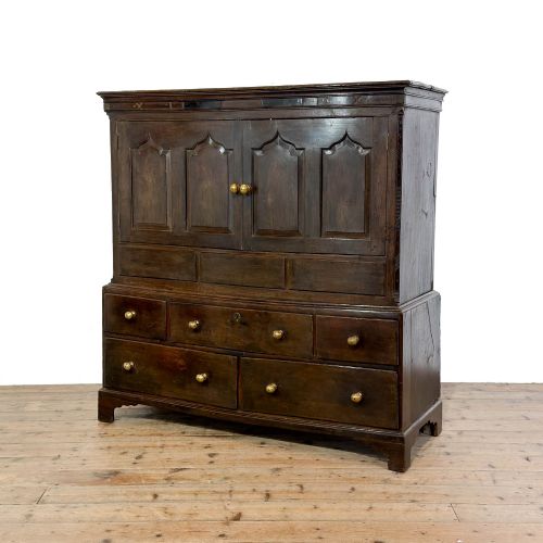 fig 1. An 18th-century Welsh dark oak Carmarthenshire coffer featuring upper cupboard doors with pointed arch fielded panels above multiple drawers fitted with brass knobs.