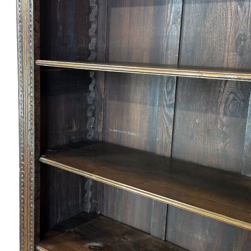 fig 1. A tall dark oak open bookcase with multiple shelves, featuring carved floral scrollwork along the top frieze and fluted side columns.