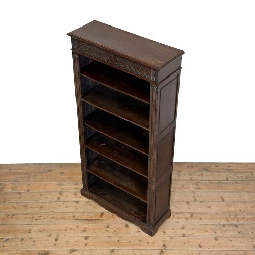 fig 2. A tall dark oak open bookcase with multiple shelves, featuring carved floral scrollwork along the top frieze and fluted side columns.