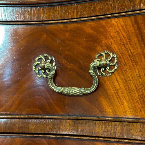 fig 3. A tall mahogany serpentine chest on chest featuring two stacked sections of graduating drawers with brass handles and carved cornice detail.
