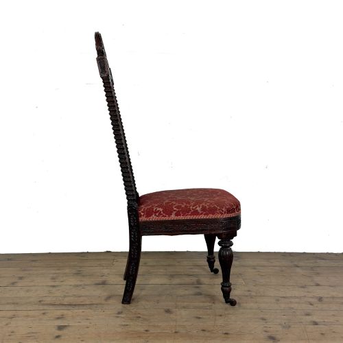 fig 1. A 19th-century Anglo-Indian chair with an intricately hand-carved lattice backrest, dark wood frame, turned legs on castors, and a patterned red upholstered seat.