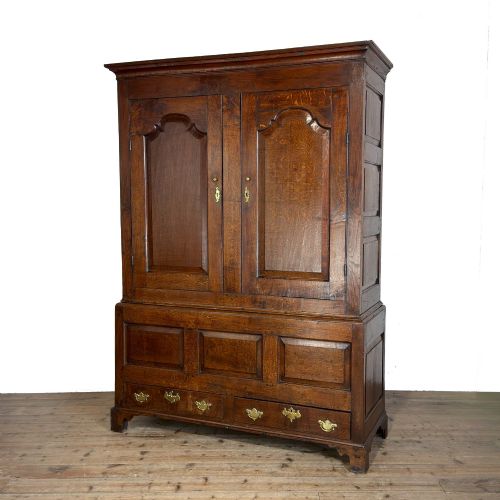 fig 1. An eighteenth-century dark oak livery cupboard featuring double arched fielded panel doors over a lower drawer base with brass handles.