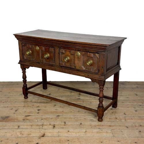 fig 1. An antique dark oak dresser base featuring two drawers with geometric raised mouldings, brass handles, turned front legs, and a low stretcher.