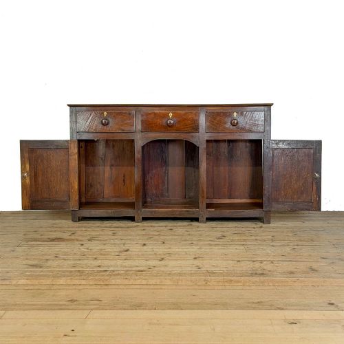 fig 1. A dark oak antique dresser base featuring three top drawers with wooden knobs and brass keyholes above two panelled cupboards flanking a central open alcove.