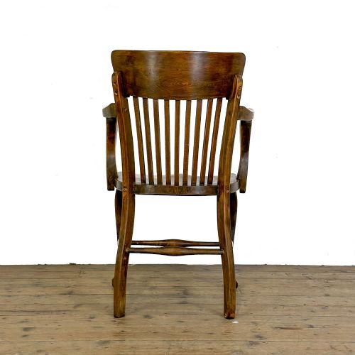 fig 1. An antique warm brown oak office armchair with a slatted backrest, curved armrests, a contoured wooden seat, and turned legs.
