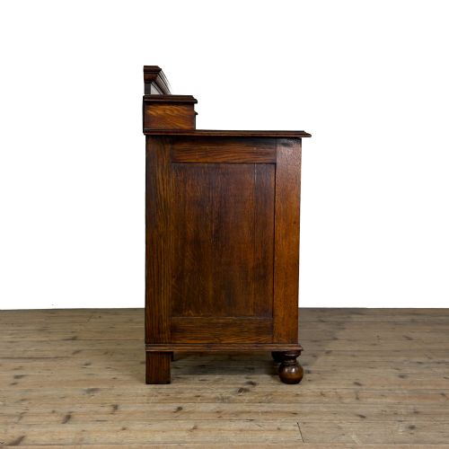 fig 2. An Arts and Crafts solid oak kneehole desk featuring a raised top gallery shelf, central drawer with geometric moulding, drop handles, and side cupboards with circular gridded glass panels.