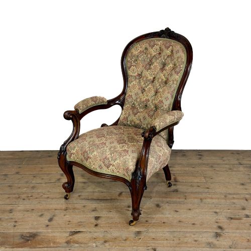 fig 1. Victorian carved mahogany armchair with deep button-backed floral tapestry upholstery, curved armrests, and cabriole legs on brass castors.