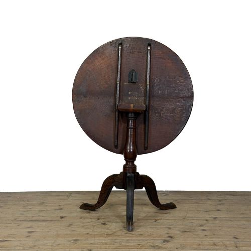 fig 2. A Georgian oak tilt top table with a circular top locked upright above a turned column pedestal and three shaped tripod legs.