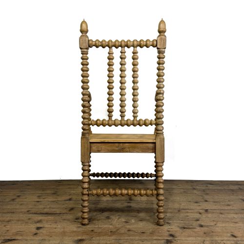 fig 1. An antique light oak armchair constructed with lathe-turned bobbin spindles along the frame, backrest, armrests, and legs, topped with carved finials.