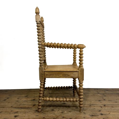 fig 2. An antique light oak armchair constructed with lathe-turned bobbin spindles along the frame, backrest, armrests, and legs, topped with carved finials.