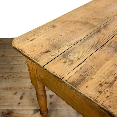fig 1. An antique stripped pine kitchen table featuring a plank top, a deep apron with corner cut-outs, and four turned legs.