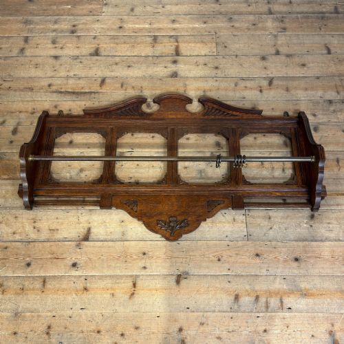 fig 1. A Victorian carved oak wall rack featuring an architectural pediment, four open rectangular frame panels, a brass hanging rod with rings, and a carved Scottish thistle motif on the lower apron.