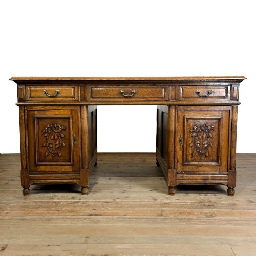 fig 1. A large antique oak partners desk featuring top drawers, carved cupboard doors on twin pedestals, metal handles, and turned bun feet.