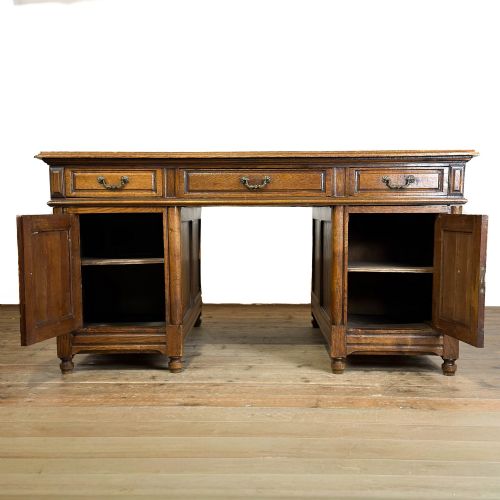 fig 2. A large antique oak partners desk featuring top drawers, carved cupboard doors on twin pedestals, metal handles, and turned bun feet.