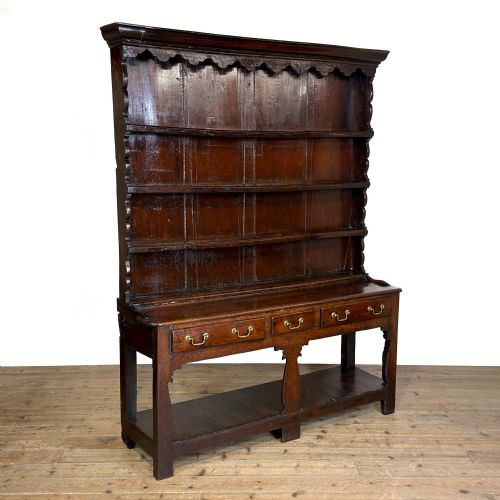 fig 1. An eighteenth-century dark oak Welsh dresser featuring an open three-tier plate rack with a scalloped top frieze over a three-drawer base with brass handles and a lower potboard shelf.