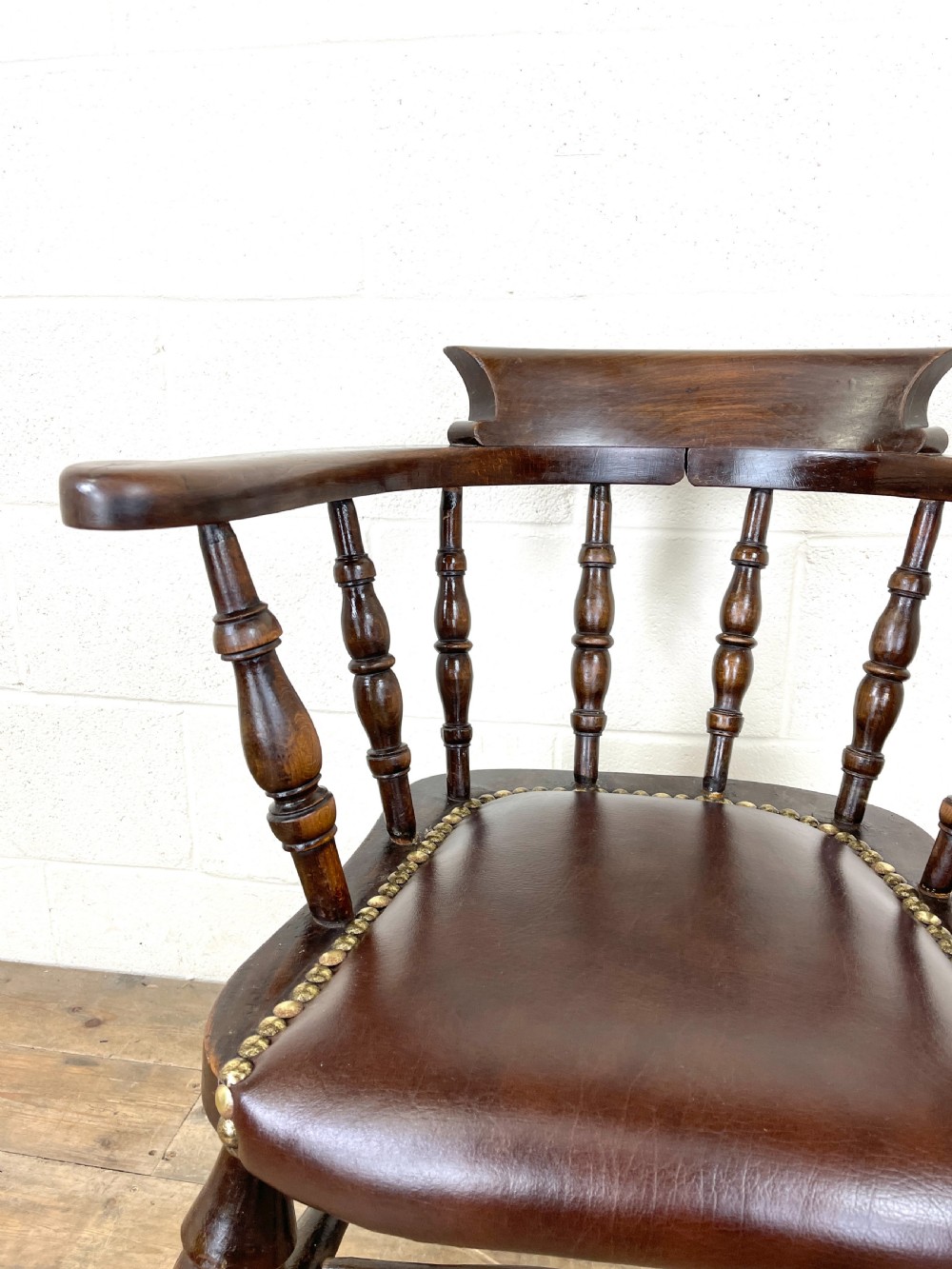 An antique dark brown wooden smokers bow armchair featuring turned spindles, a curved top rail, and a brown leather upholstered seat secured with brass studs. View IV