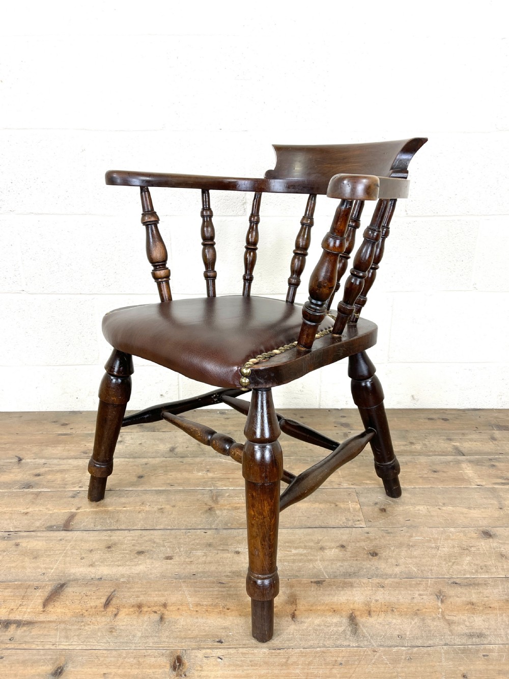 An antique dark brown wooden smokers bow armchair featuring turned spindles, a curved top rail, and a brown leather upholstered seat secured with brass studs. View VI