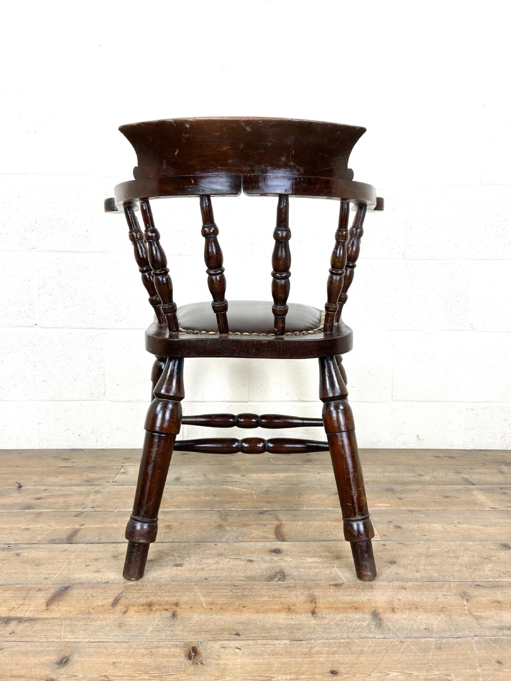 An antique dark brown wooden smokers bow armchair featuring turned spindles, a curved top rail, and a brown leather upholstered seat secured with brass studs. View VII
