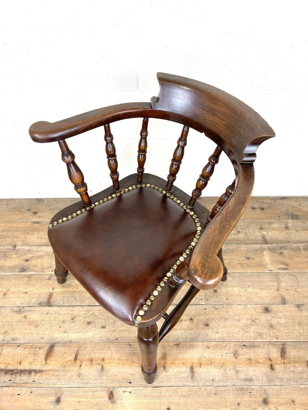 An antique dark brown wooden smokers bow armchair featuring turned spindles, a curved top rail, and a brown leather upholstered seat secured with brass studs. View VIII