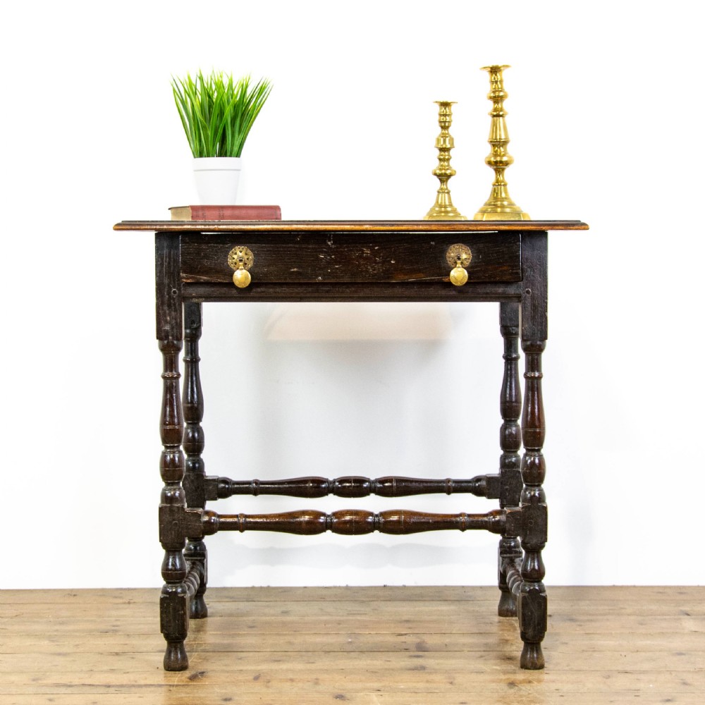 A dark elm side table featuring turned legs, horizontal turned stretchers, and a single drawer with brass drop handles.