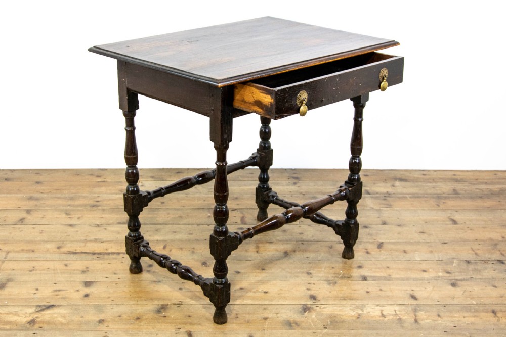 A dark elm side table featuring turned legs, horizontal turned stretchers, and a single drawer with brass drop handles. View VII