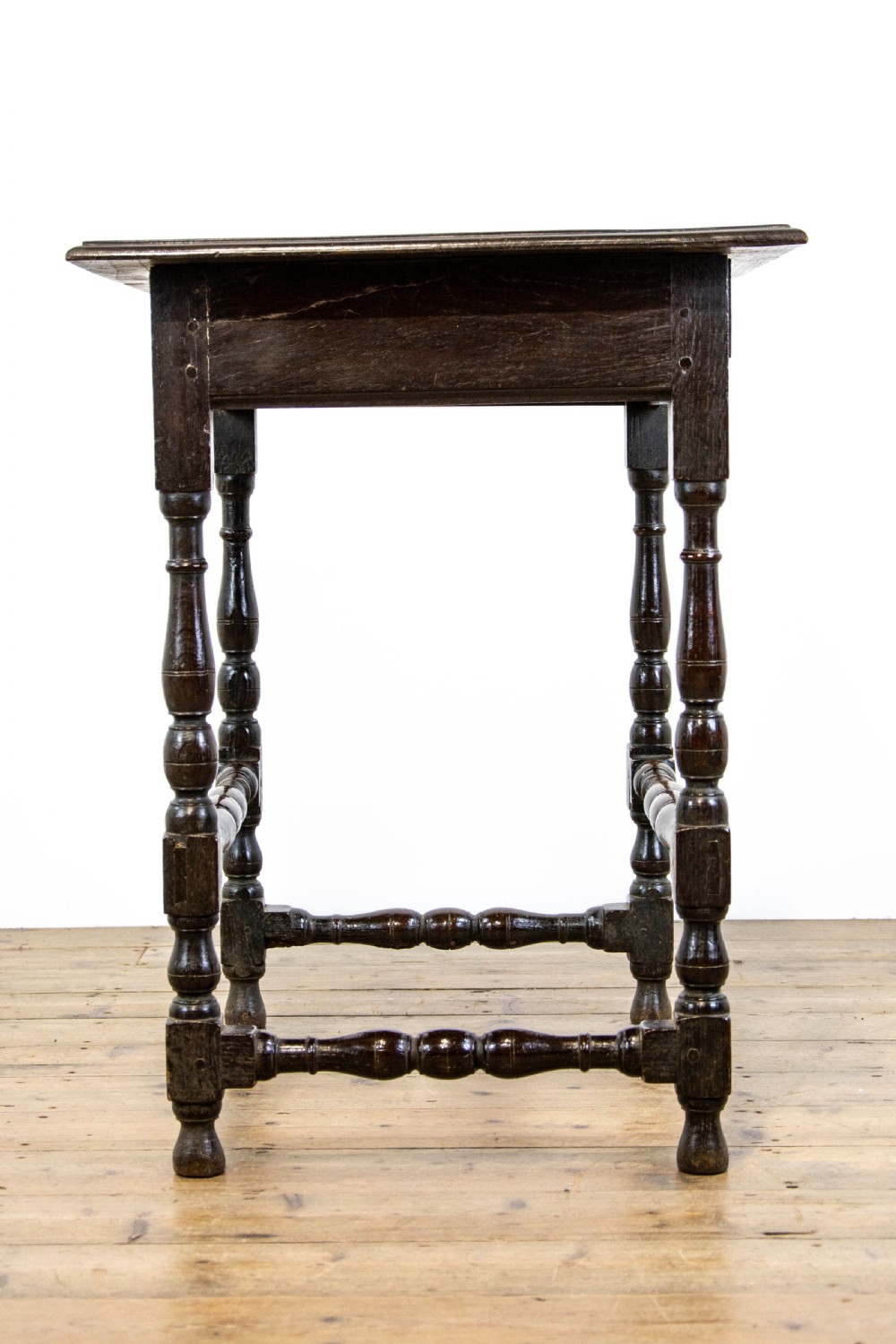 A dark elm side table featuring turned legs, horizontal turned stretchers, and a single drawer with brass drop handles. View VIII
