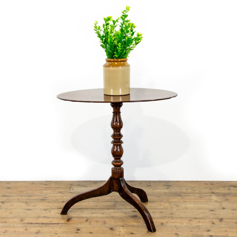 An antique mahogany side table featuring an oval top supported by a turned central pedestal and three curved tripod legs.