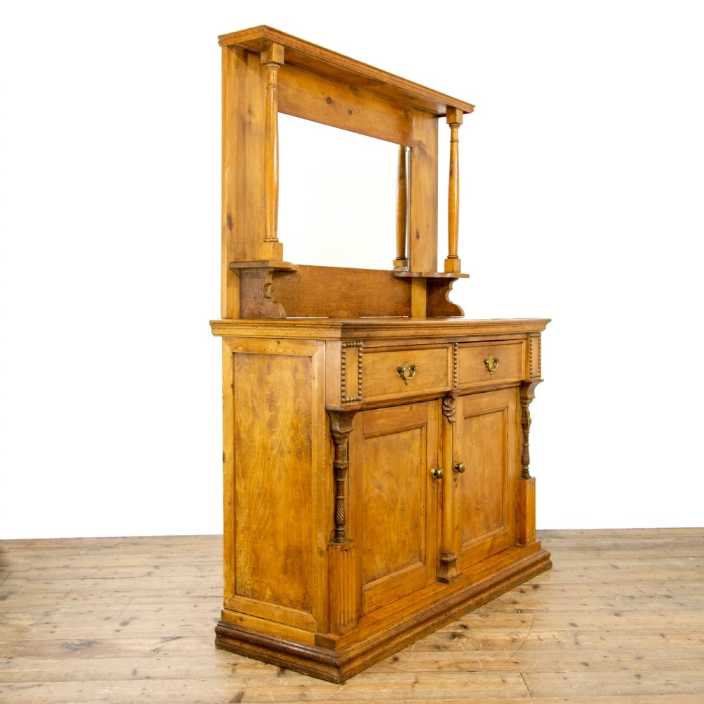 A light oak and pine sideboard featuring a raised mirror back with turned columns, two upper drawers, and a two-door lower cupboard.