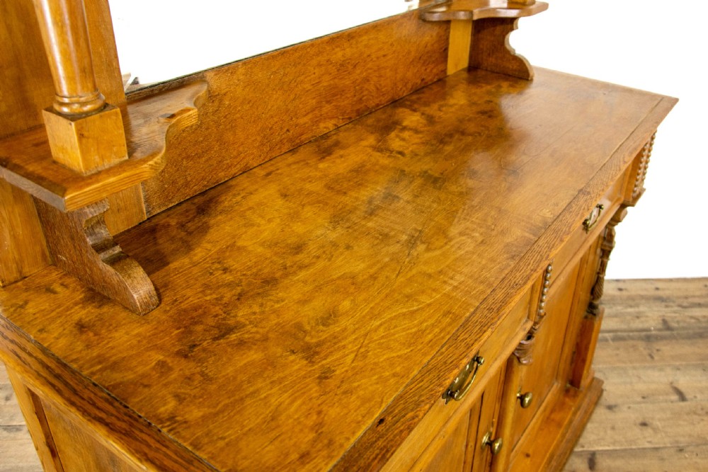 A light oak and pine sideboard featuring a raised mirror back with turned columns, two upper drawers, and a two-door lower cupboard. View VII