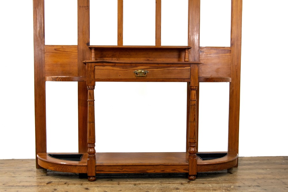 A tall Victorian pitch pine hall stand featuring a central mirror, brass coat hooks, a small drawer unit, and integrated umbrella racks with drip trays. View III