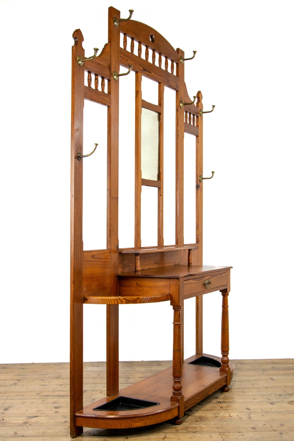 A tall Victorian pitch pine hall stand featuring a central mirror, brass coat hooks, a small drawer unit, and integrated umbrella racks with drip trays. View IX
