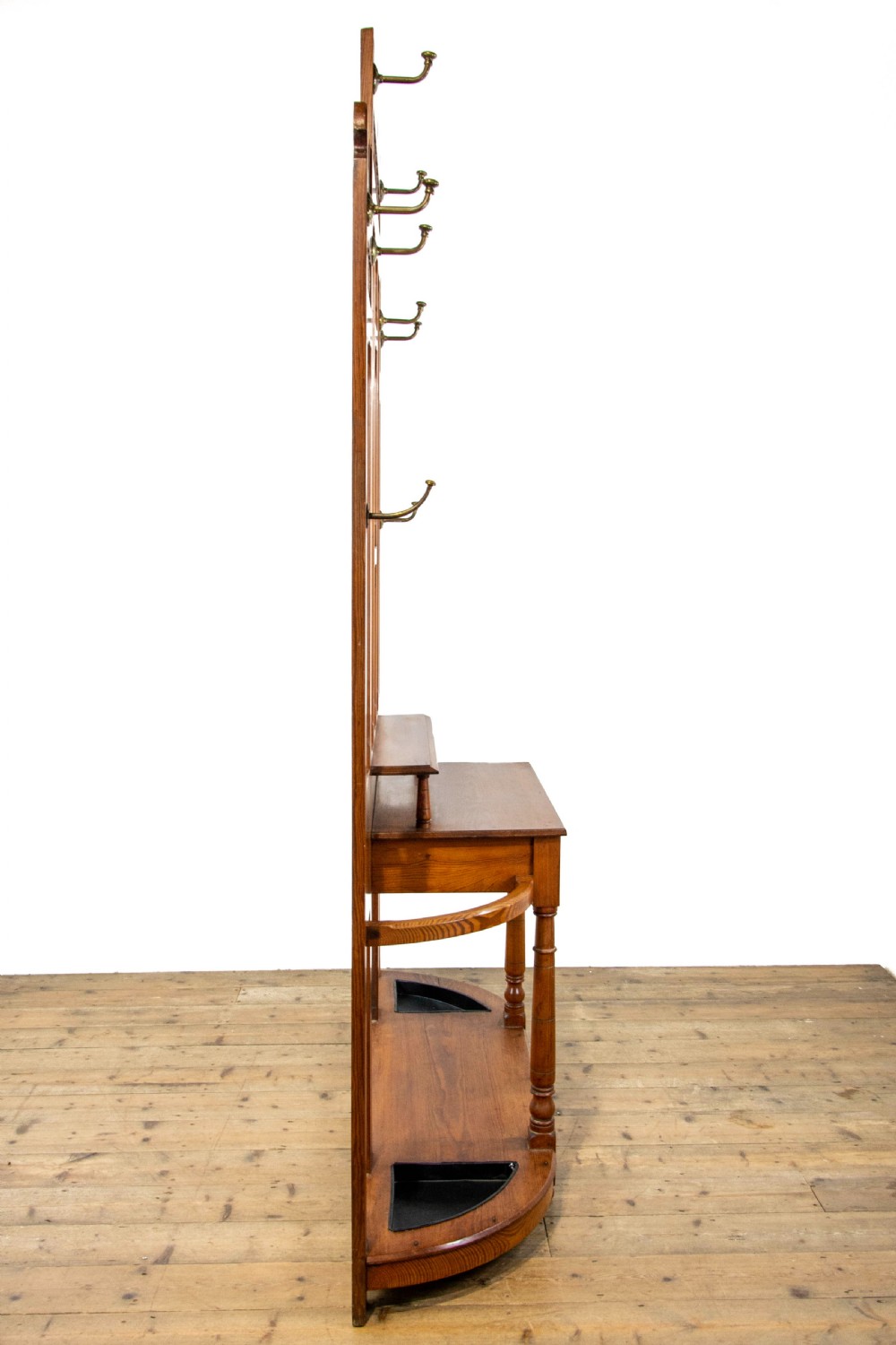 A tall Victorian pitch pine hall stand featuring a central mirror, brass coat hooks, a small drawer unit, and integrated umbrella racks with drip trays. View XI