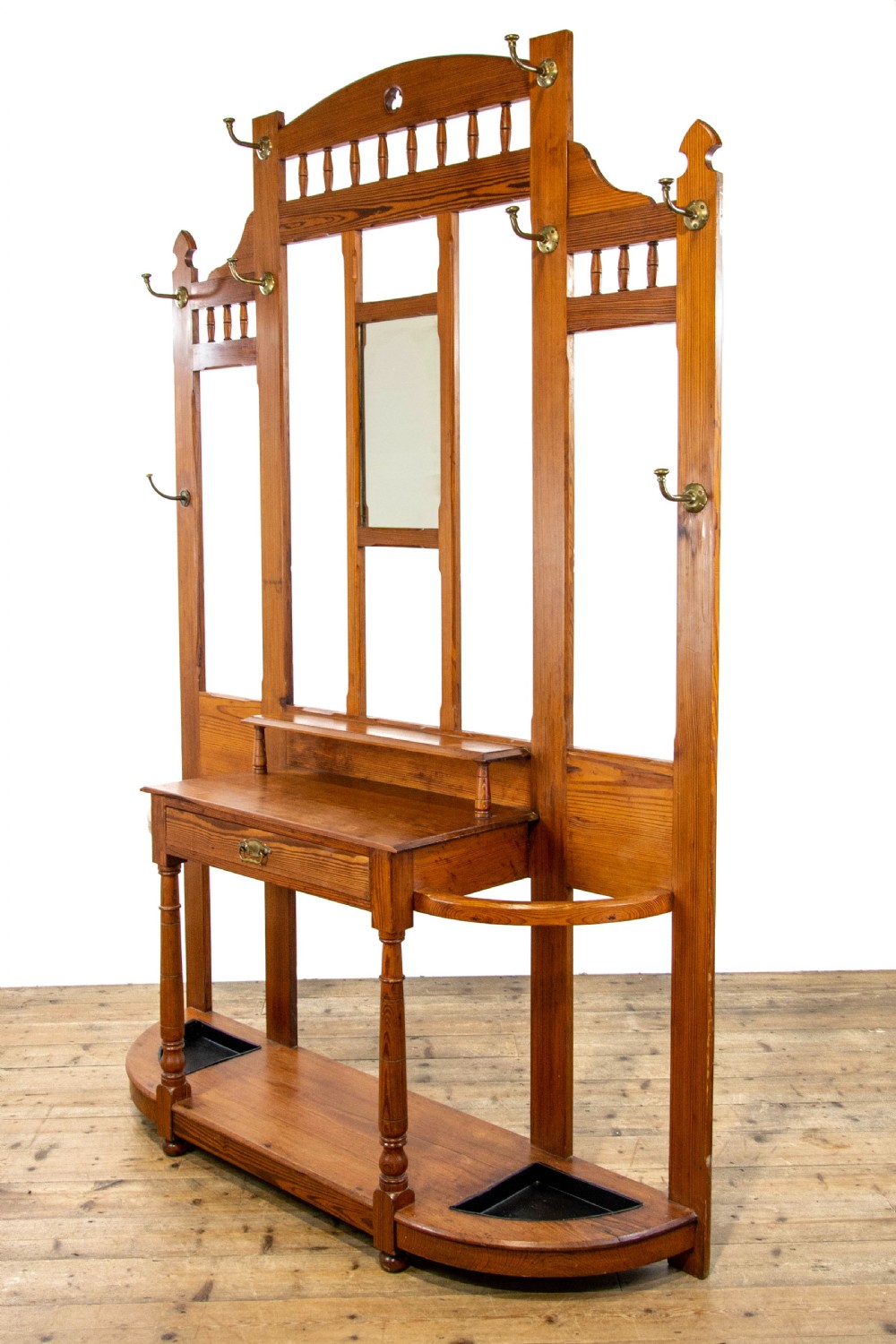 A tall Victorian pitch pine hall stand featuring a central mirror, brass coat hooks, a small drawer unit, and integrated umbrella racks with drip trays. View XIII