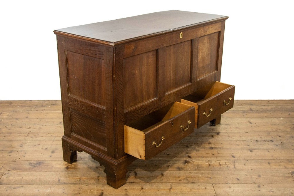 An antique dark oak mule chest featuring three recessed front panels, two lower drawers with brass swan-neck handles, and bracket feet. View VI