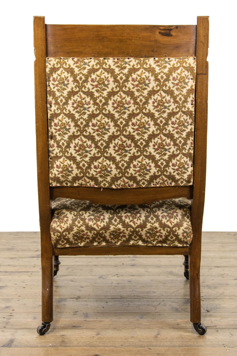 An antique Edwardian low-slung chair featuring a carved timber frame, patterned textile upholstery, turned front legs, and castors. View IX