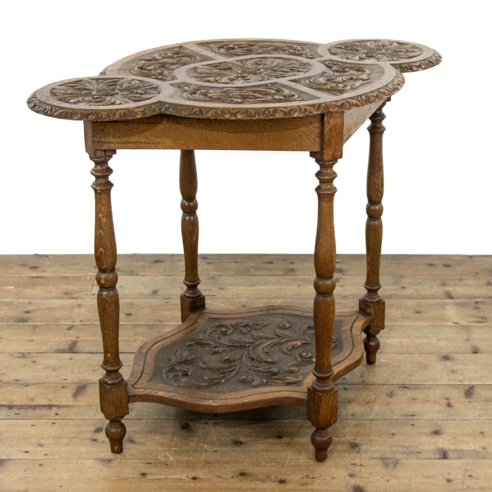 A carved oak side table featuring a lobed, relief-carved top with floral motifs, four turned legs, and a carved lower tier shelf.