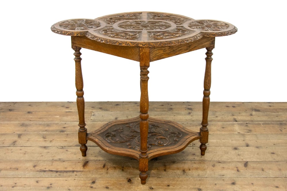 A carved oak side table featuring a lobed, relief-carved top with floral motifs, four turned legs, and a carved lower tier shelf. View III