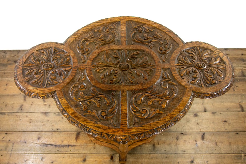 A carved oak side table featuring a lobed, relief-carved top with floral motifs, four turned legs, and a carved lower tier shelf. View V