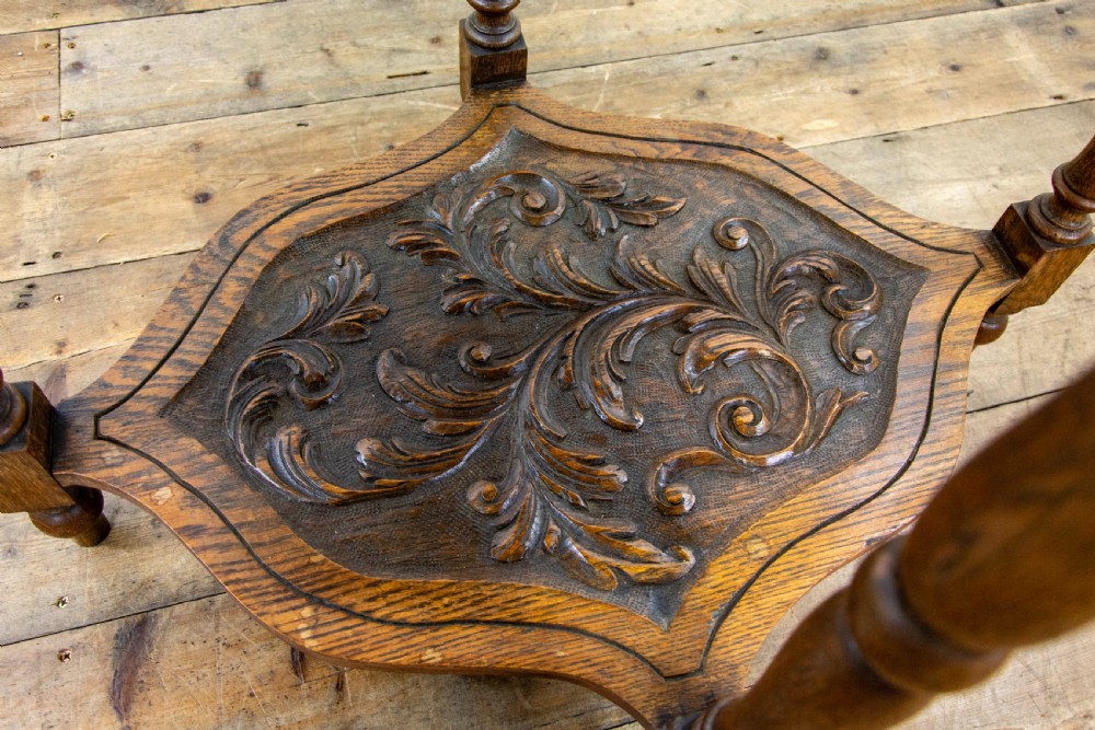 A carved oak side table featuring a lobed, relief-carved top with floral motifs, four turned legs, and a carved lower tier shelf. View VI