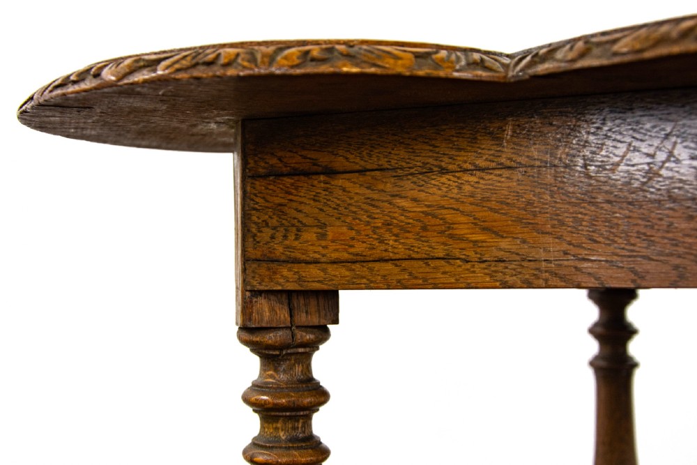 A carved oak side table featuring a lobed, relief-carved top with floral motifs, four turned legs, and a carved lower tier shelf. View VII
