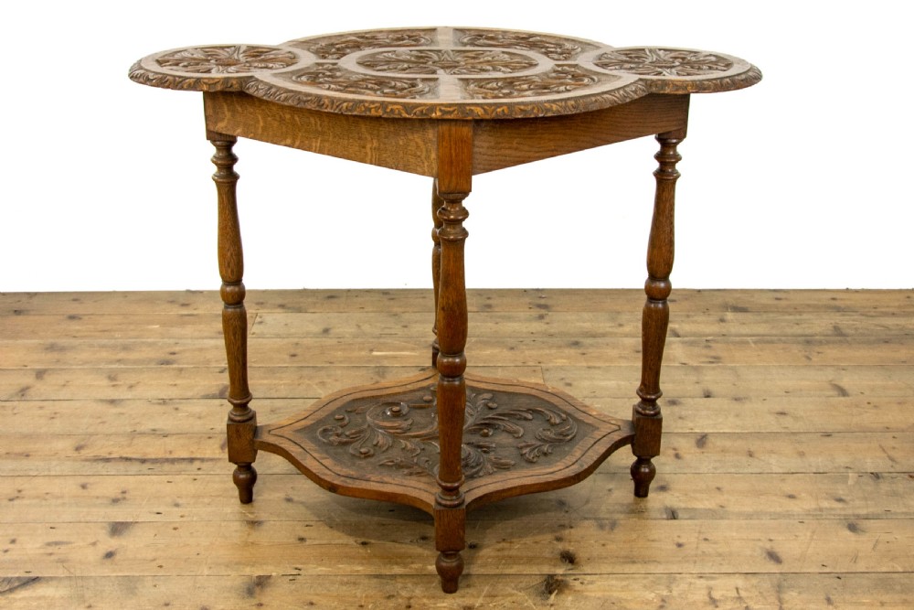 A carved oak side table featuring a lobed, relief-carved top with floral motifs, four turned legs, and a carved lower tier shelf. View IX